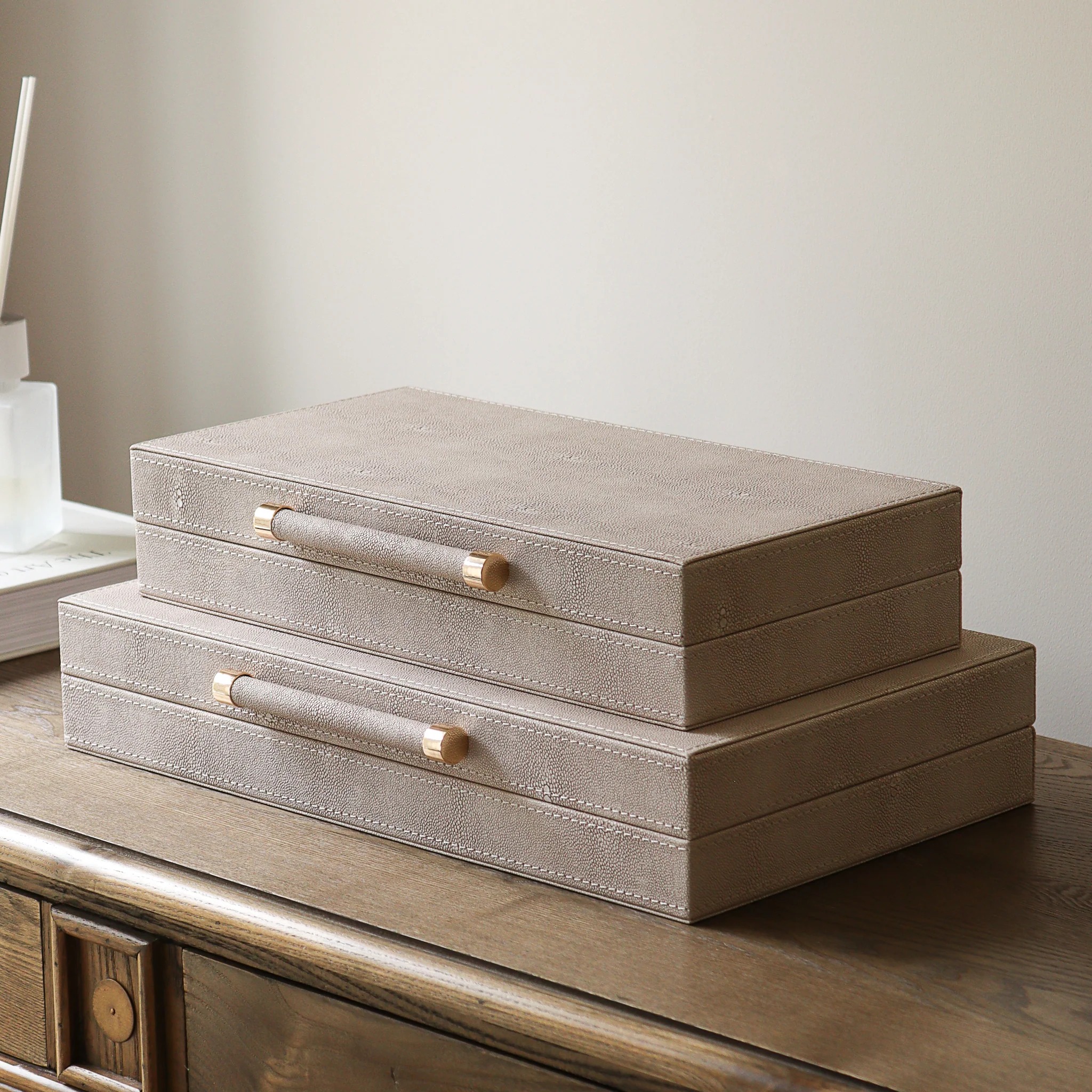 Two stacked beige faux shagreen decorative boxes with gold handles | Al Janah Al Malaky